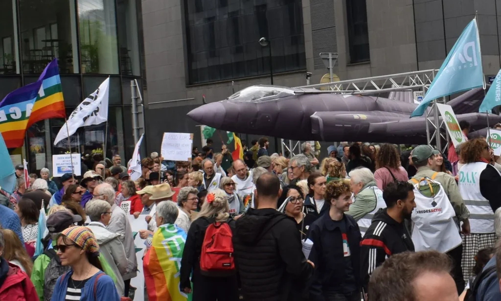 Demonstrierende Personen auf der Straße, ein aufblasbarer Militärjet im Hintergrund